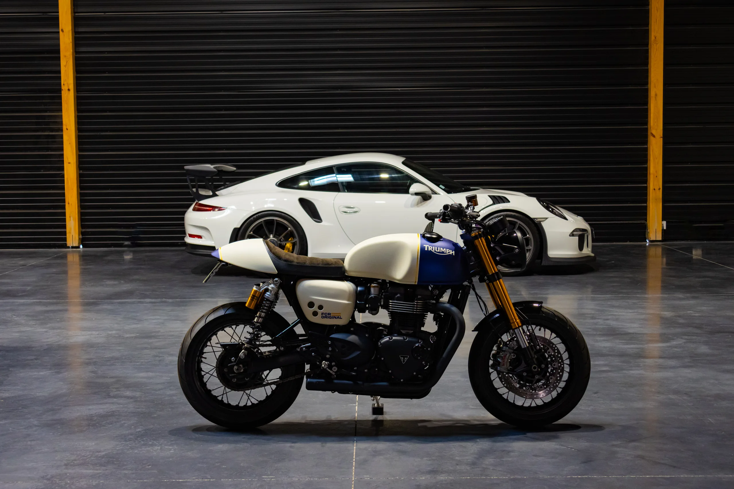 Triumph Thruxton Roadster Classic FCR Original crème et bleue devant une Porsche 911 blanche