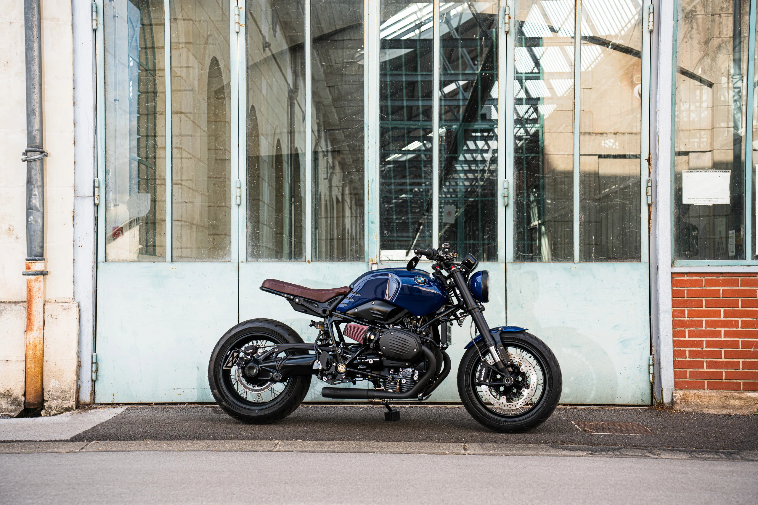 BMW R nineT Urban FCR Original bleue garée devant une porte d'atelier vitrée