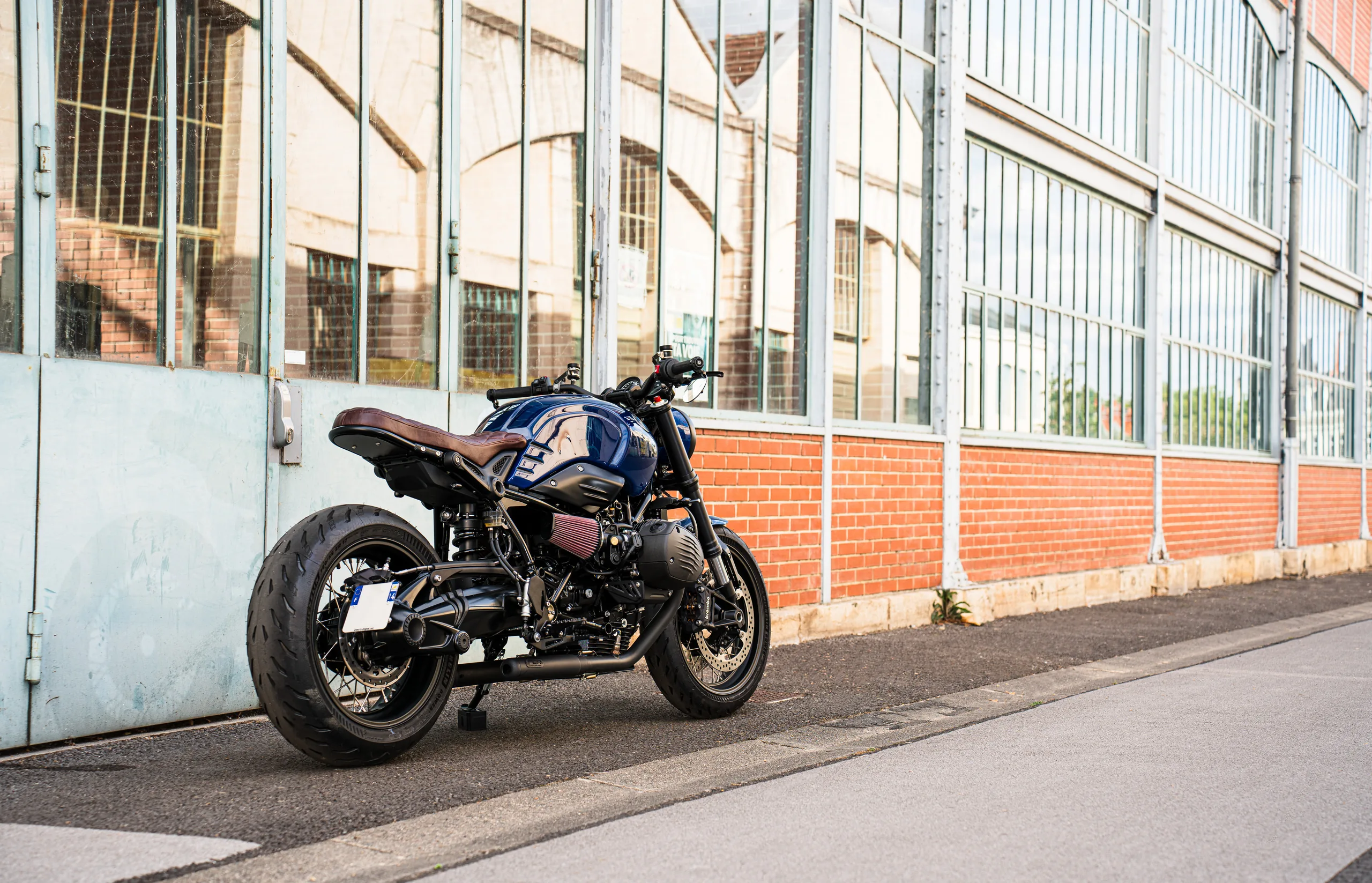 Vue arrière trois quarts d'une BMW R nineT Urban FCR Original bleue devant un mur de briques