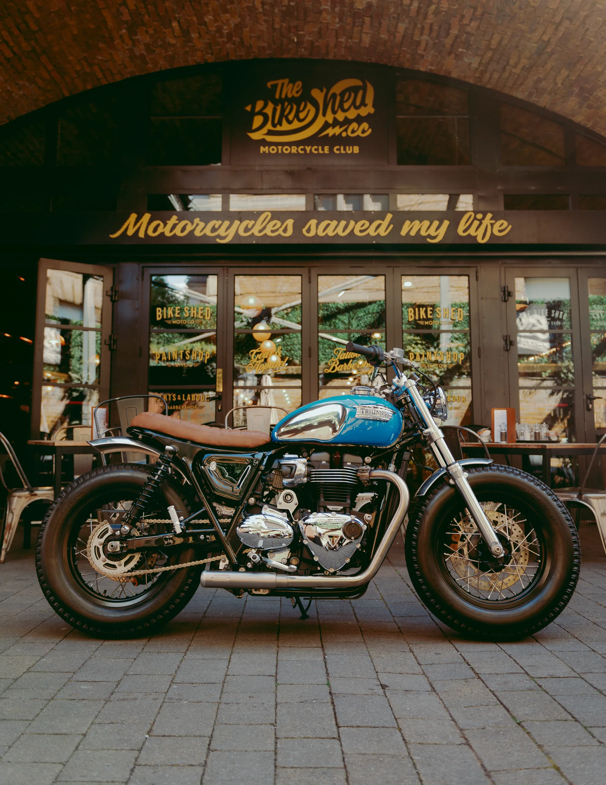 Triumph Fat Bike FCR Original turquoise avec selle marron devant le Bike Shed Motorcycle Club à Londres