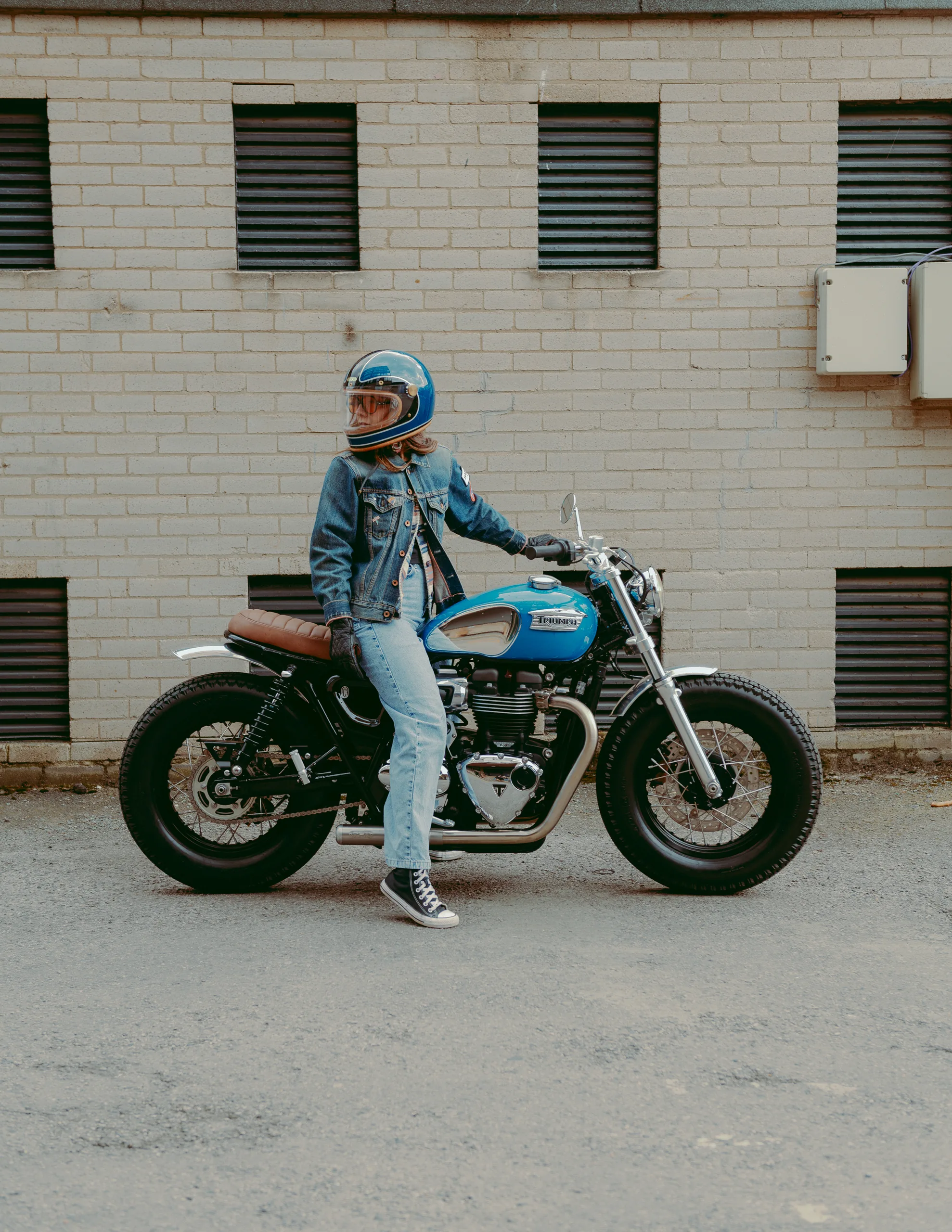 Motard en veste en jean et casque bleu sur une Triumph Fat Bike FCR Original turquoise