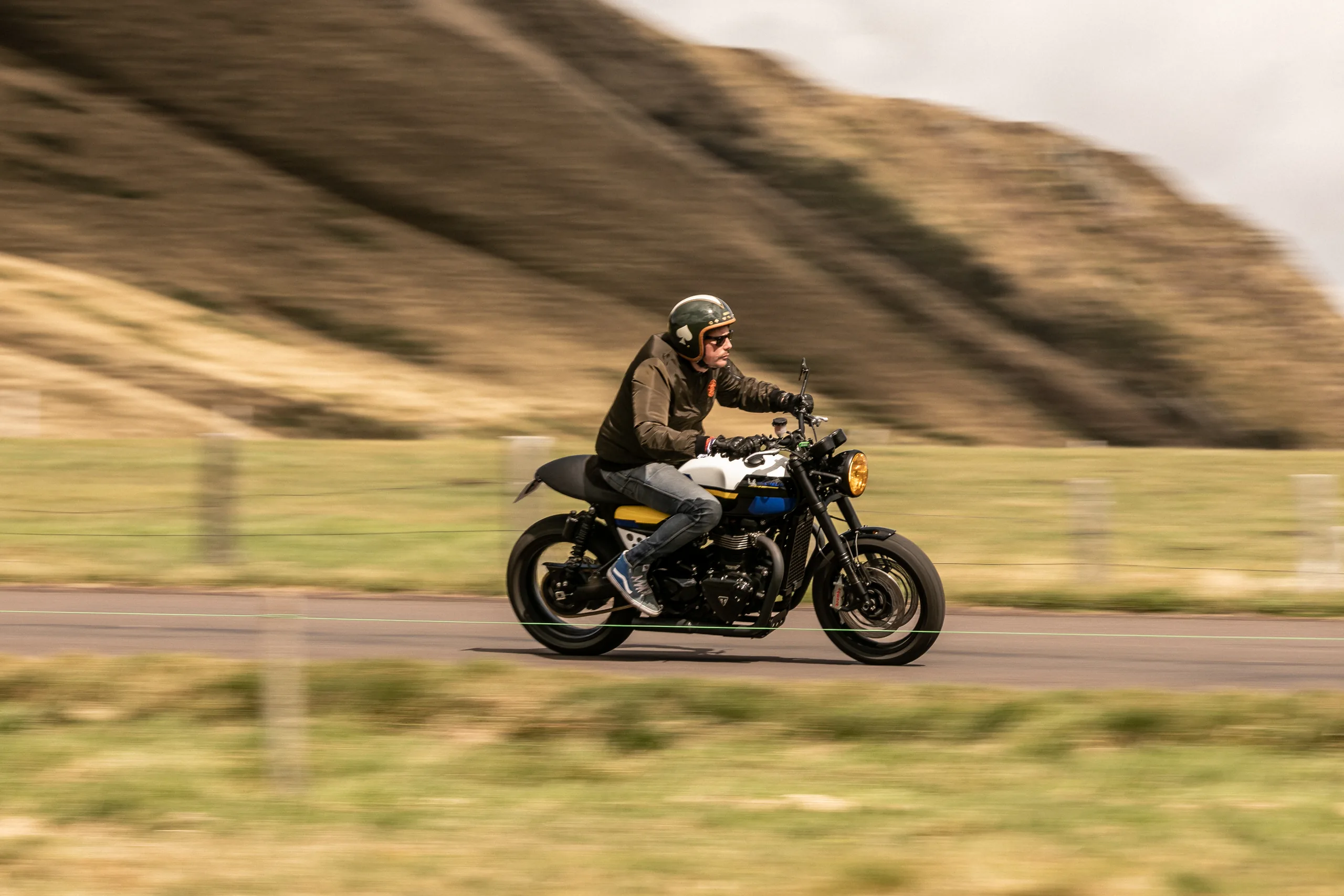 Motard roulant en Triumph Thruxton Roadster Classic FCR Original sur une route de colline