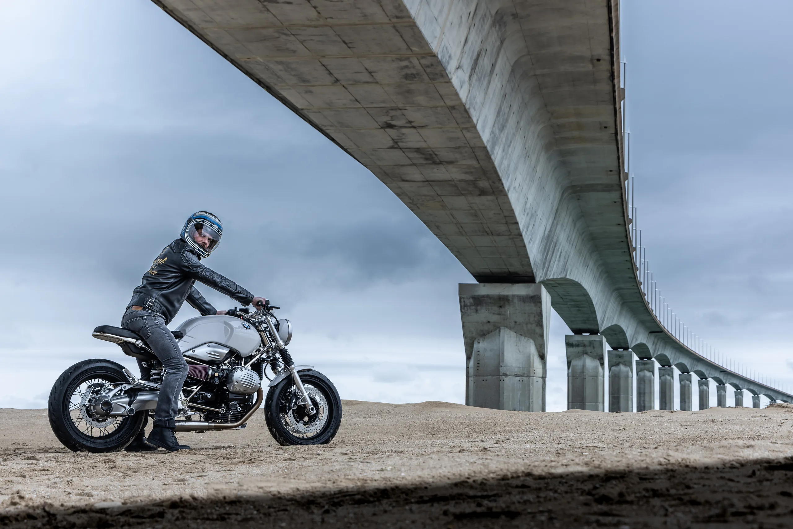 Pilote sur une BMW R nineT Urban FCR Original grise, arrêté sous un pont en béton