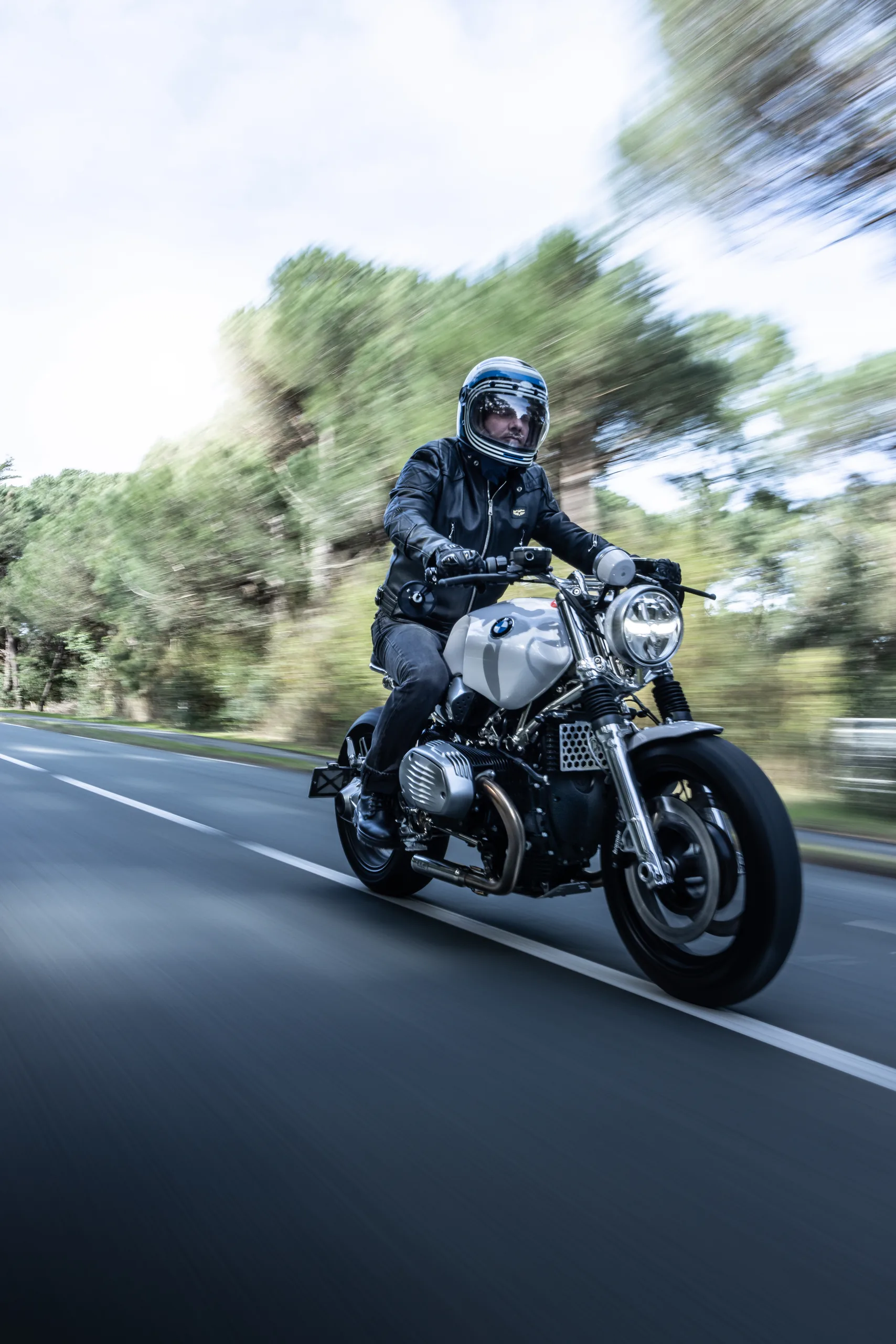 Pilote en blouson cuir roulant sur route de campagne en BMW R nineT Urban FCR Original