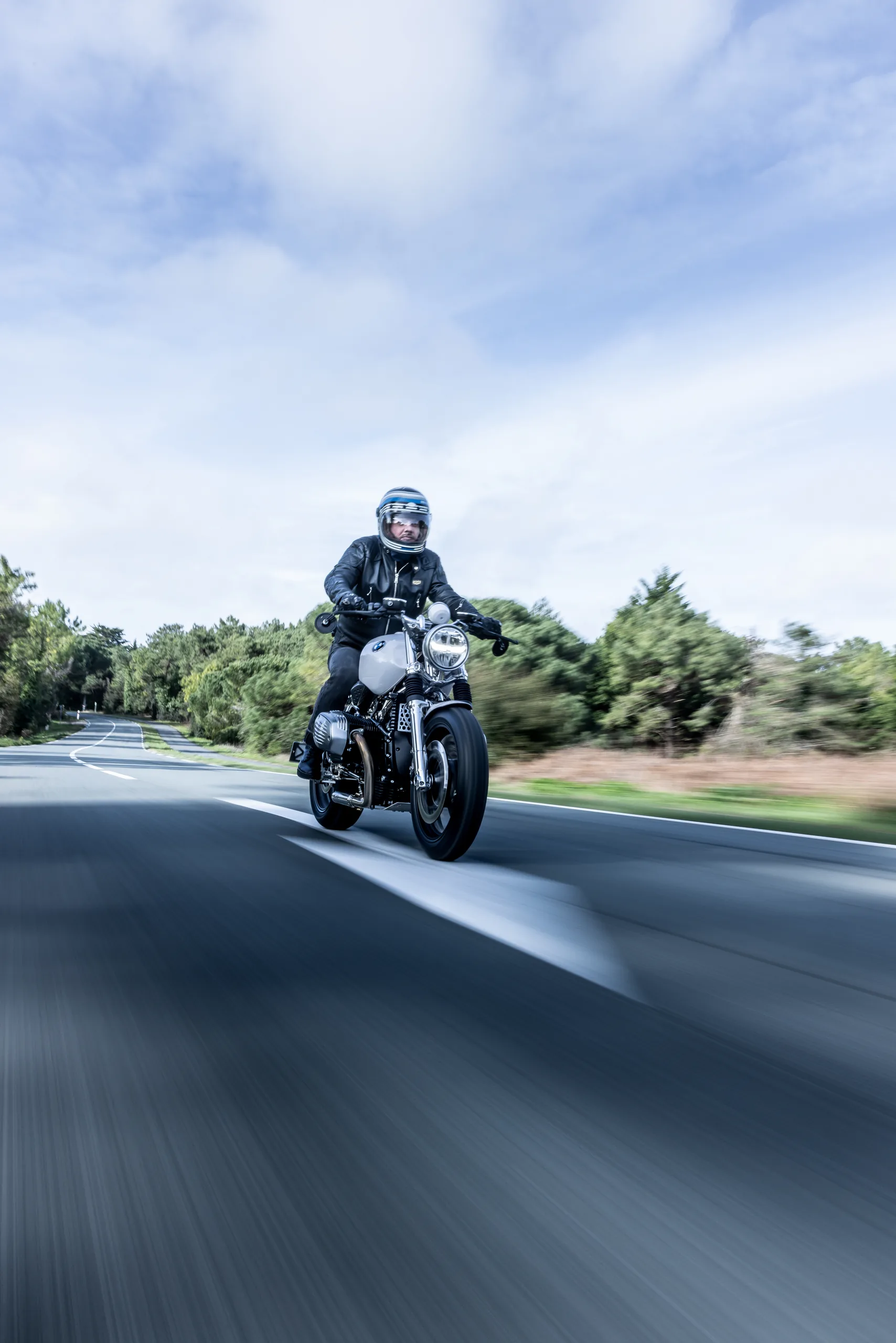 Pilote en BMW R nineT Urban FCR Original grise sur une route bordée d'arbres