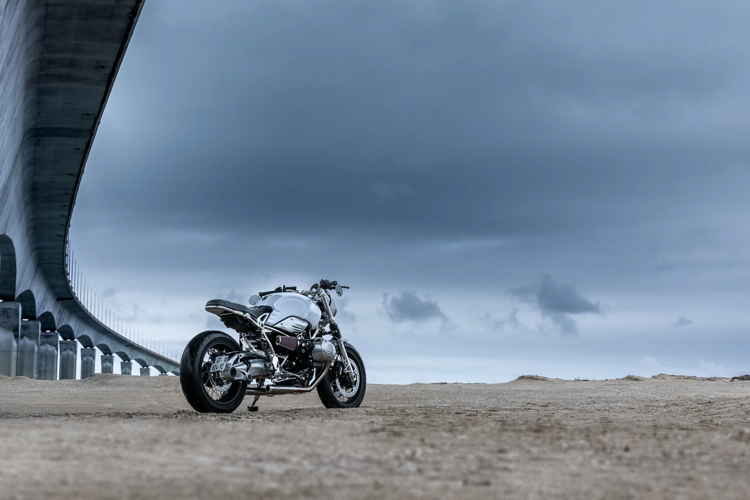 BMW R nineT Urban FCR Original grise sous un pont en béton par ciel nuageux