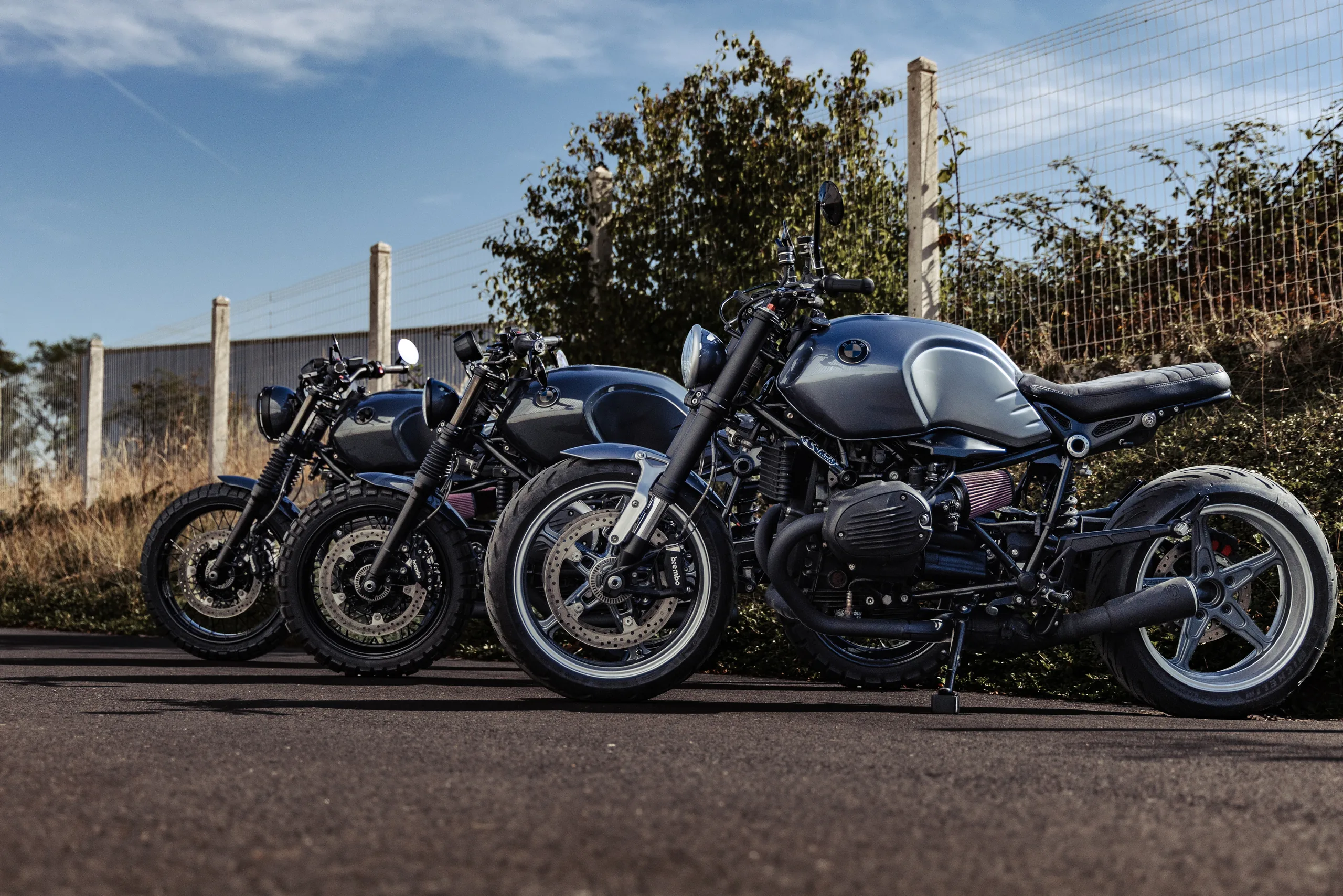 Trois BMW R nineT Urban FCR Original grises alignées devant un grillage, jantes à bâtons et freins Brembo