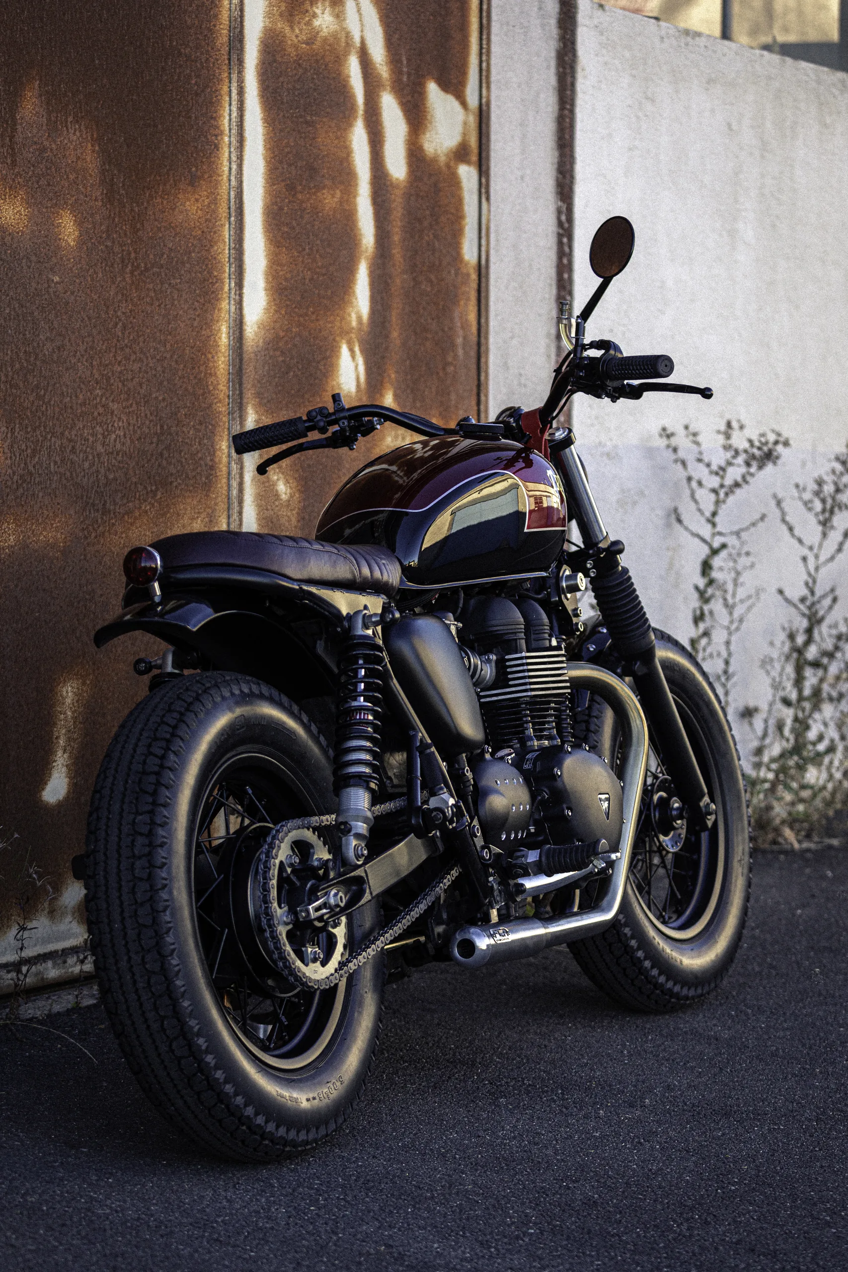 Triumph Fat Bike FCR Original bordeaux vue de trois quarts devant un mur rouillé
