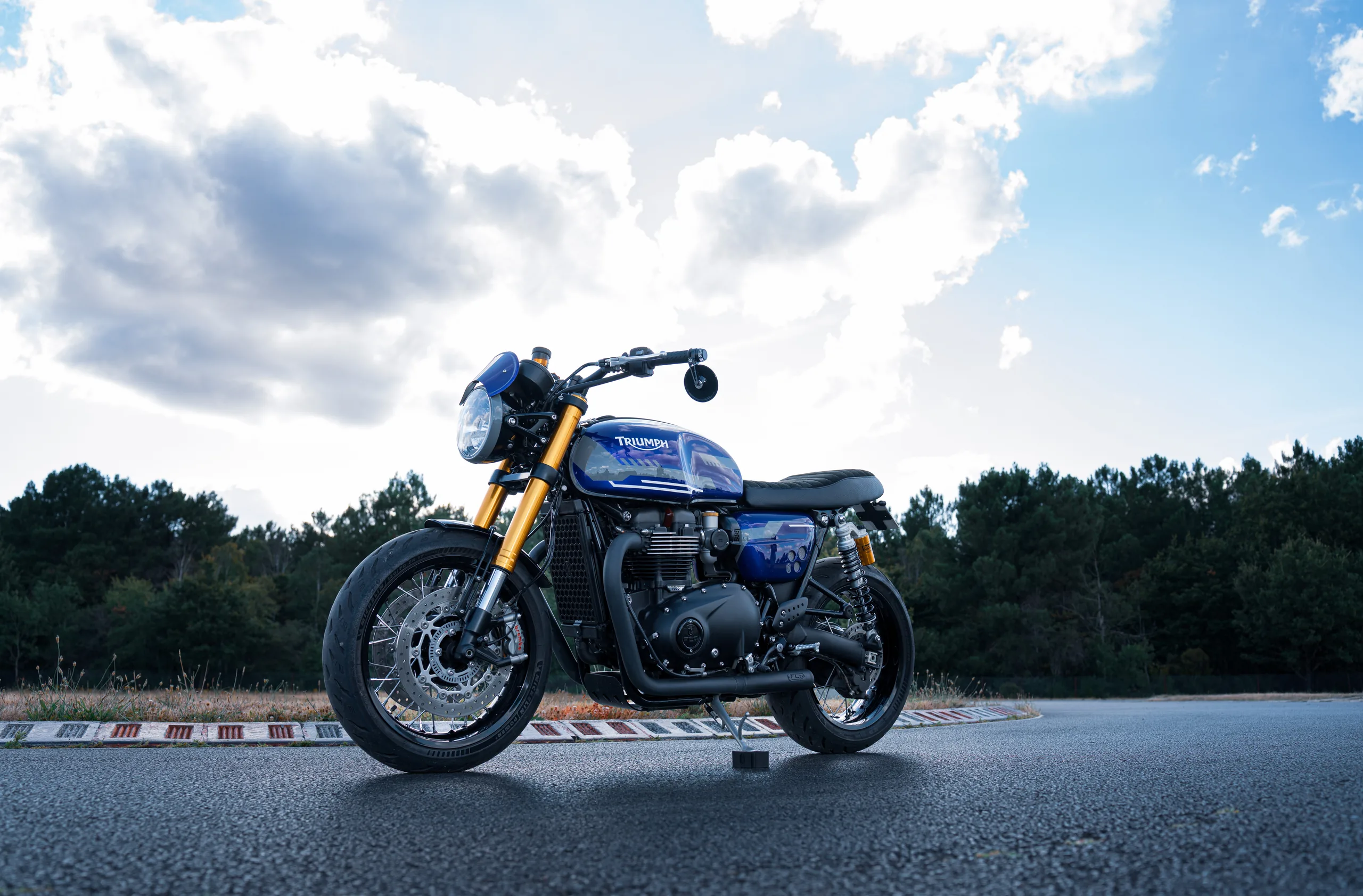 Triumph Thruxton RS Roadster Classic FCR Original bleu violine avec fourche dorée sur un circuit
