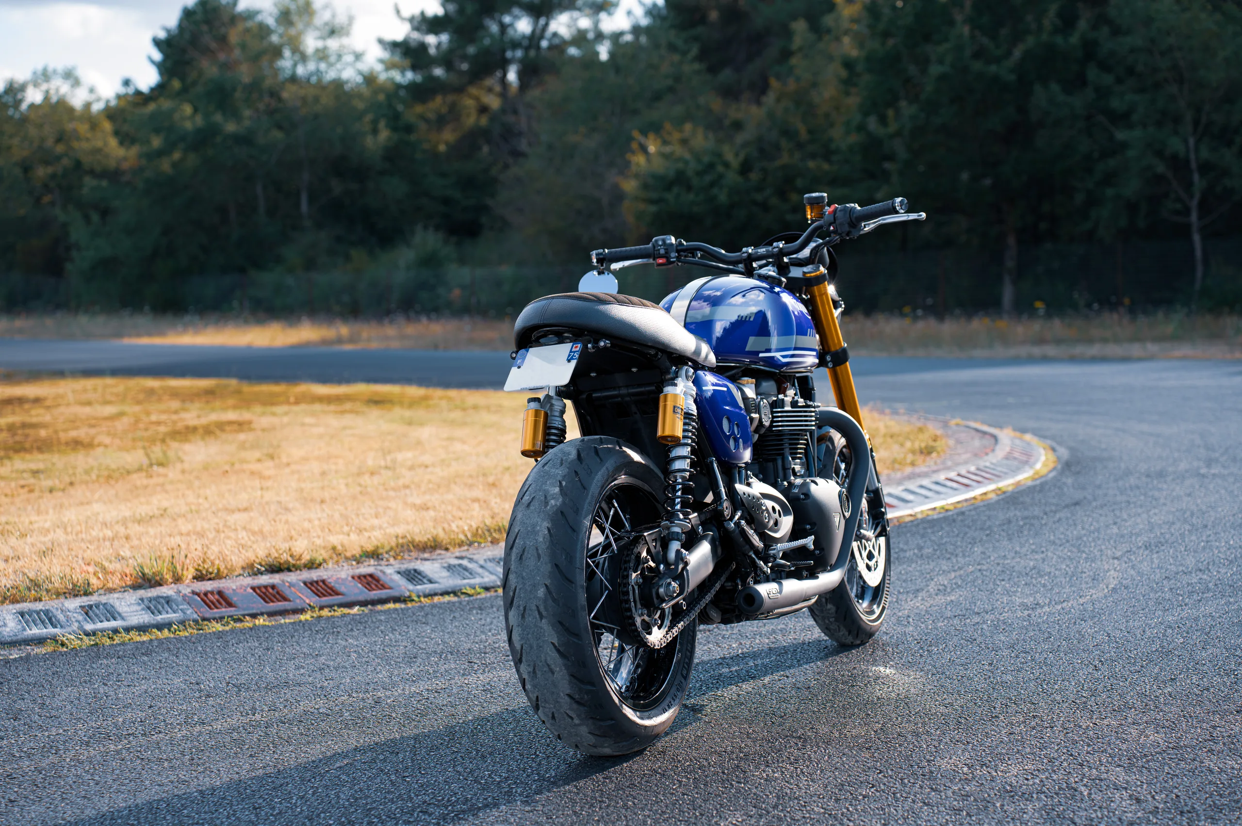 Vue arrière d'une Triumph Thruxton RS Roadster Classic FCR Original bleue sur un circuit