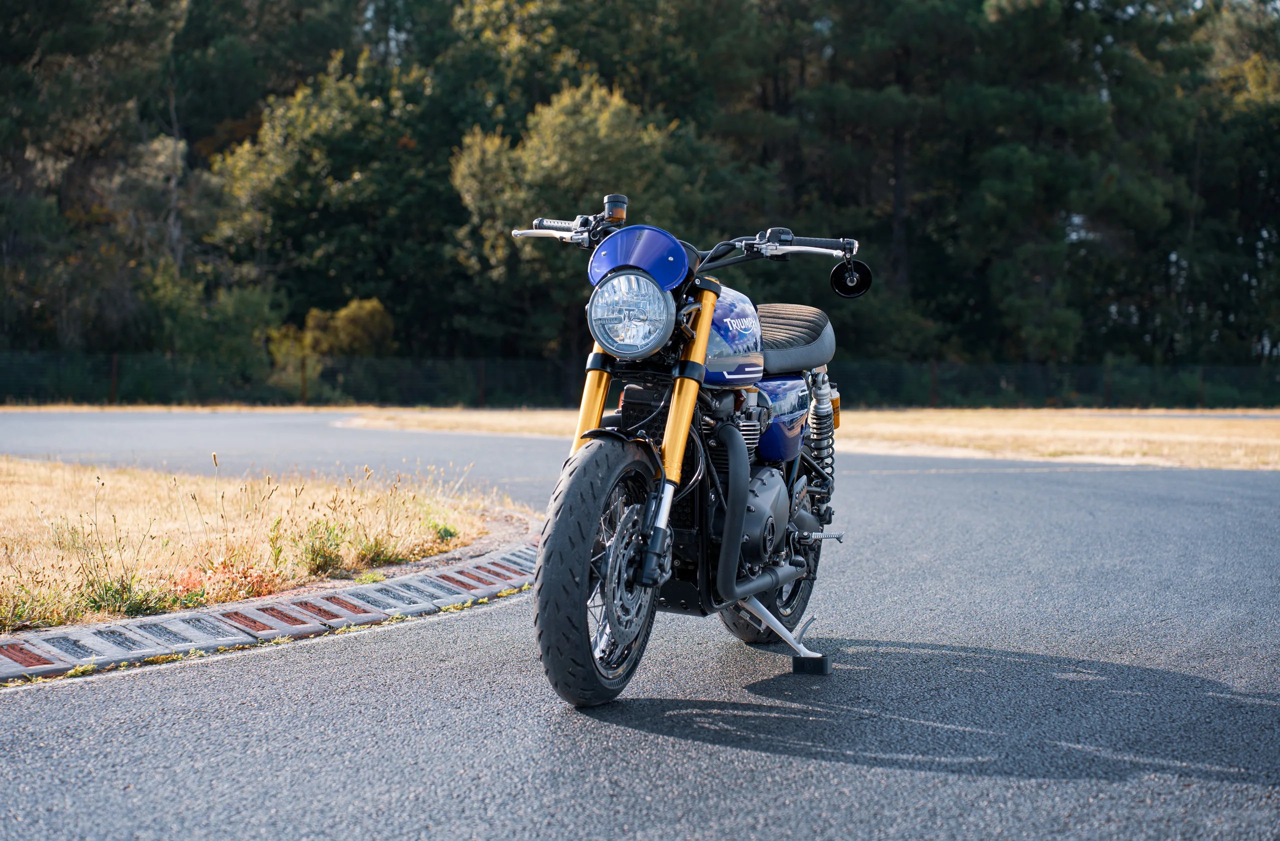 Vue avant d'une Triumph Thruxton RS Roadster Classic FCR Original bleue avec fourche dorée sur circuit