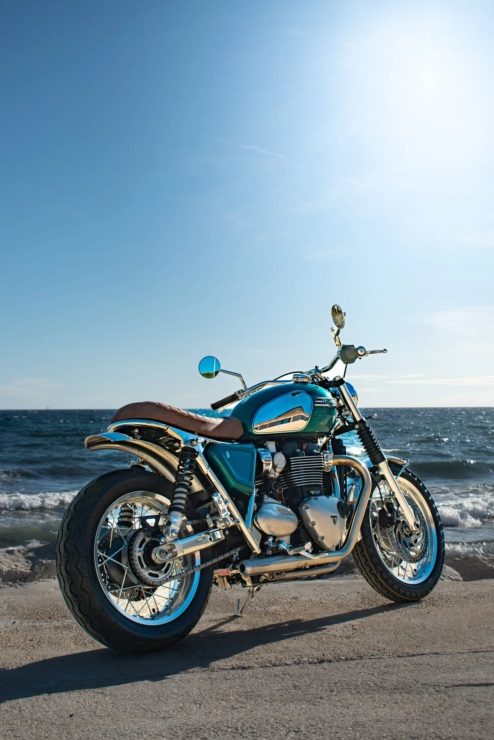 Triumph Ride & Chrome FCR Original turquoise avec selle marron garée face à la mer