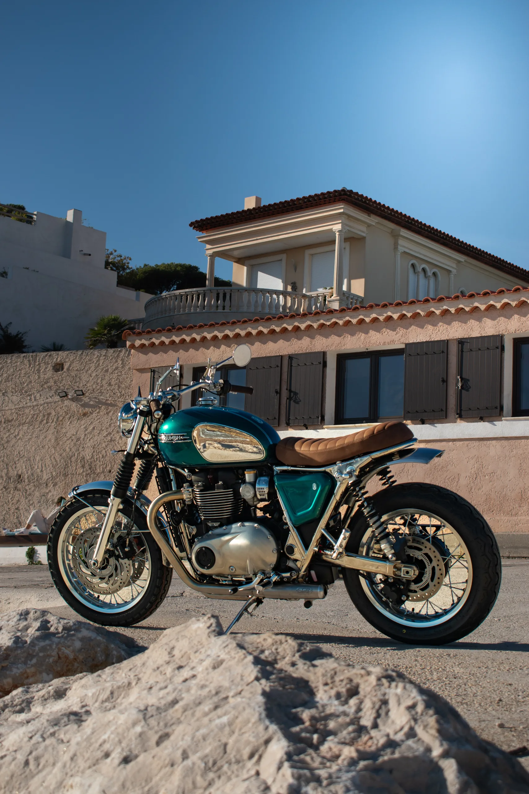Triumph Ride & Chrome FCR Original turquoise avec selle marron devant une villa ensoleillée