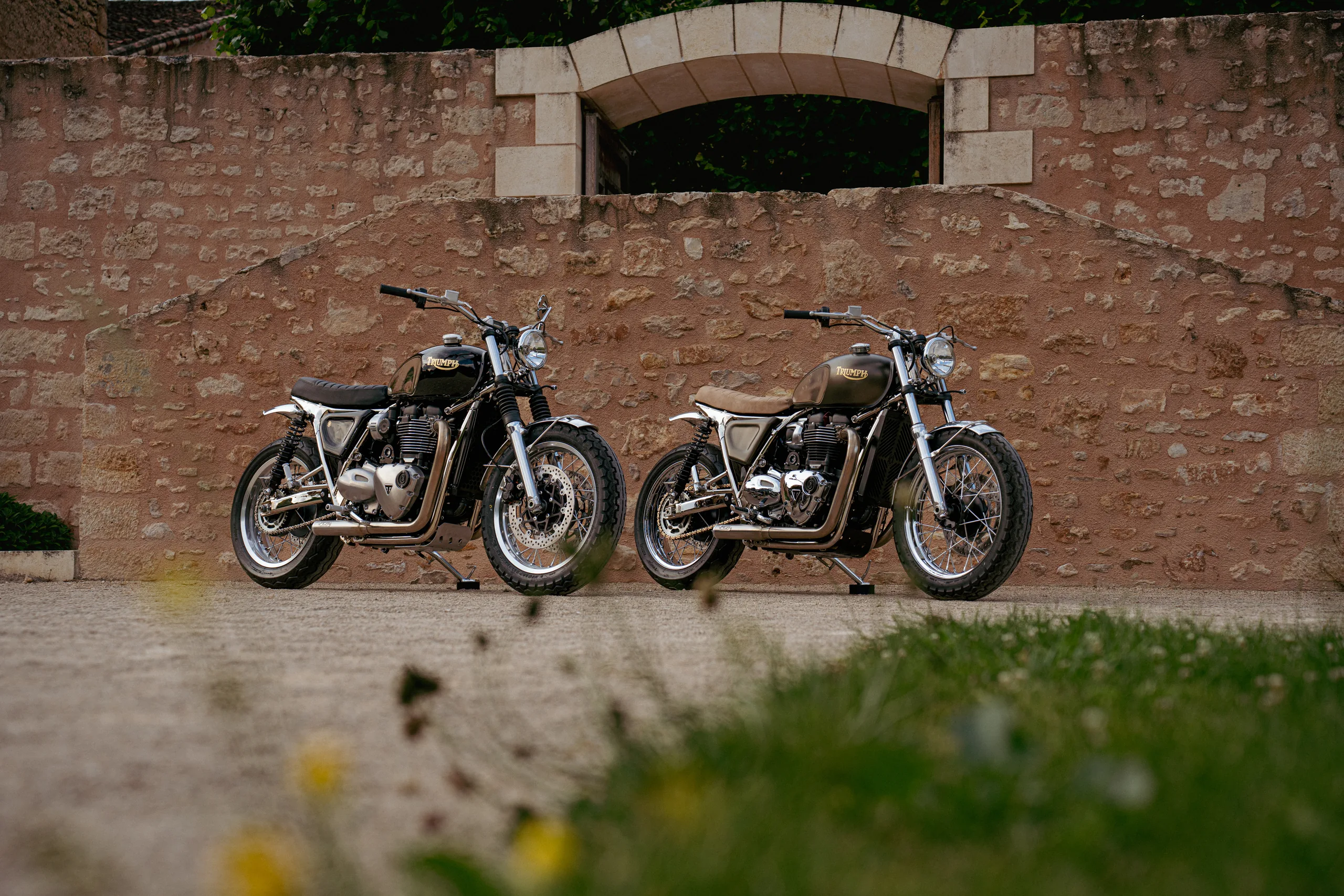 Deux Triumph Ride & Chrome FCR Original garées au pied d'un mur en pierre ancien