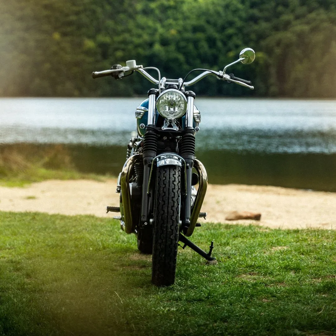 Découvrez la Triumph Speed Twin bleue vintage, une moto rétro devant un beau lac. Avec son design élégant et ses accents chromés, elle séduit les amateurs de motos classiques et de paysages naturels.