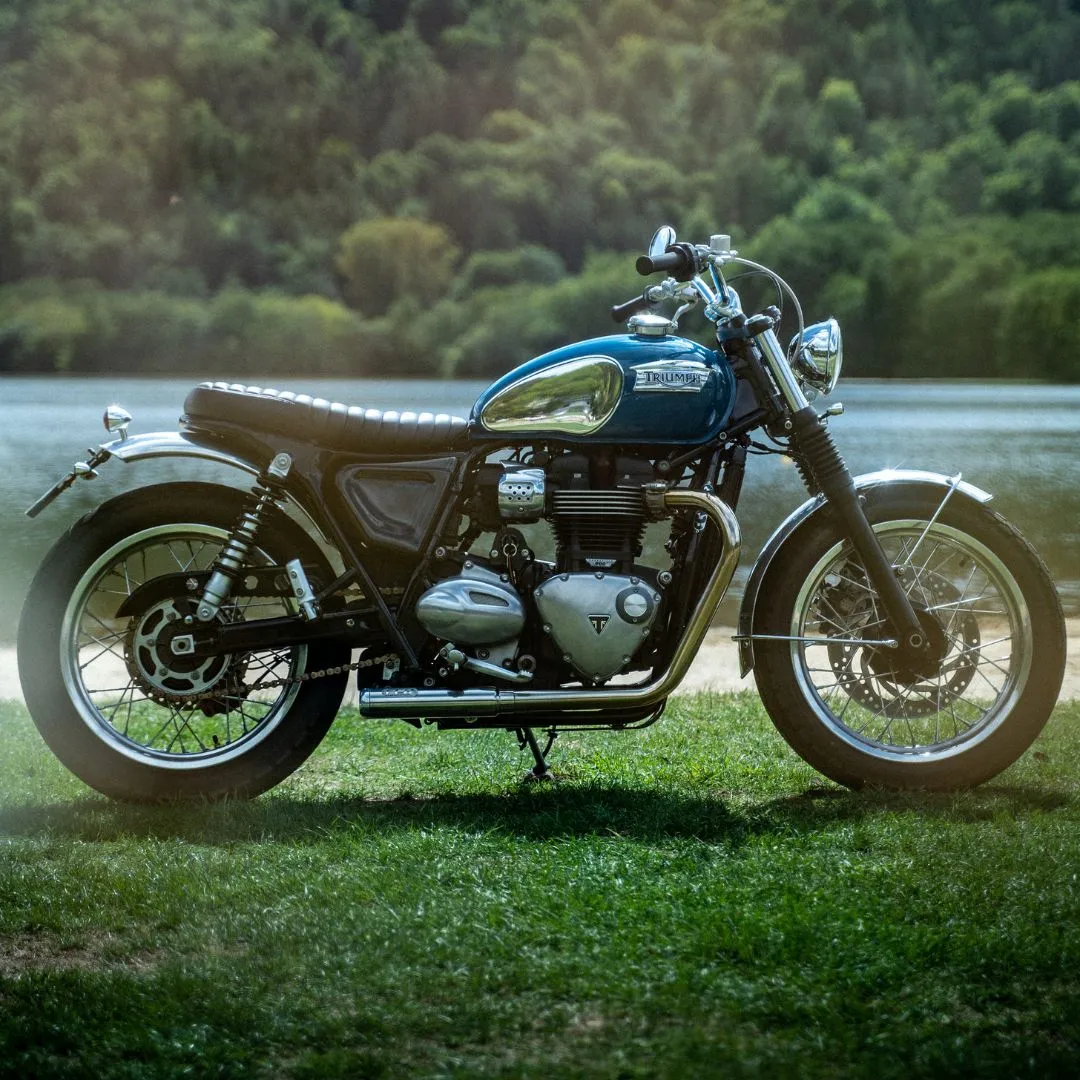 Découvrez la Triumph Speed Twin bleue vintage, photographiée devant un beau lac. Son design rétro et ses détails chromés en font une moto parfaite pour les amateurs de vintage et de nature.