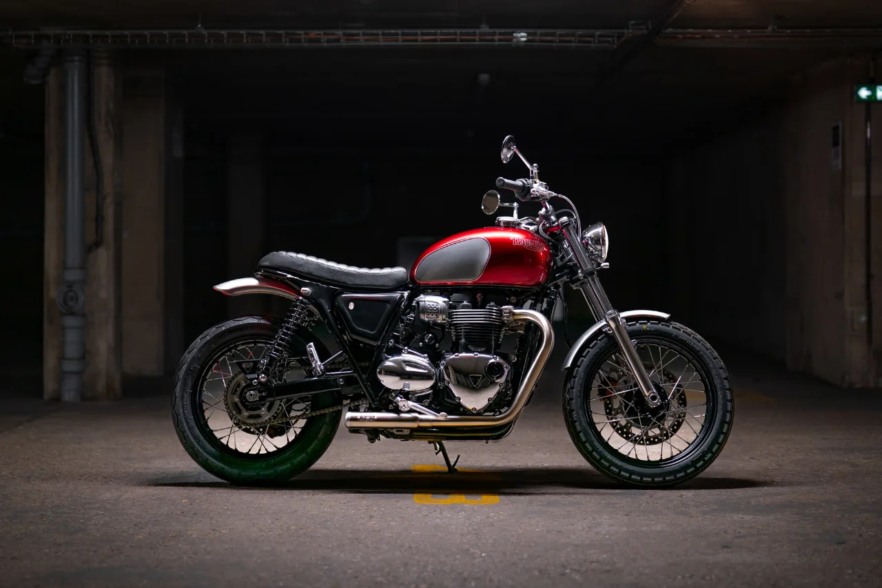 Triumph T100 Bordeaux Red — moto d’occasion 2025, préparation FCR Original, finitions chromées et réservoir bicolore.