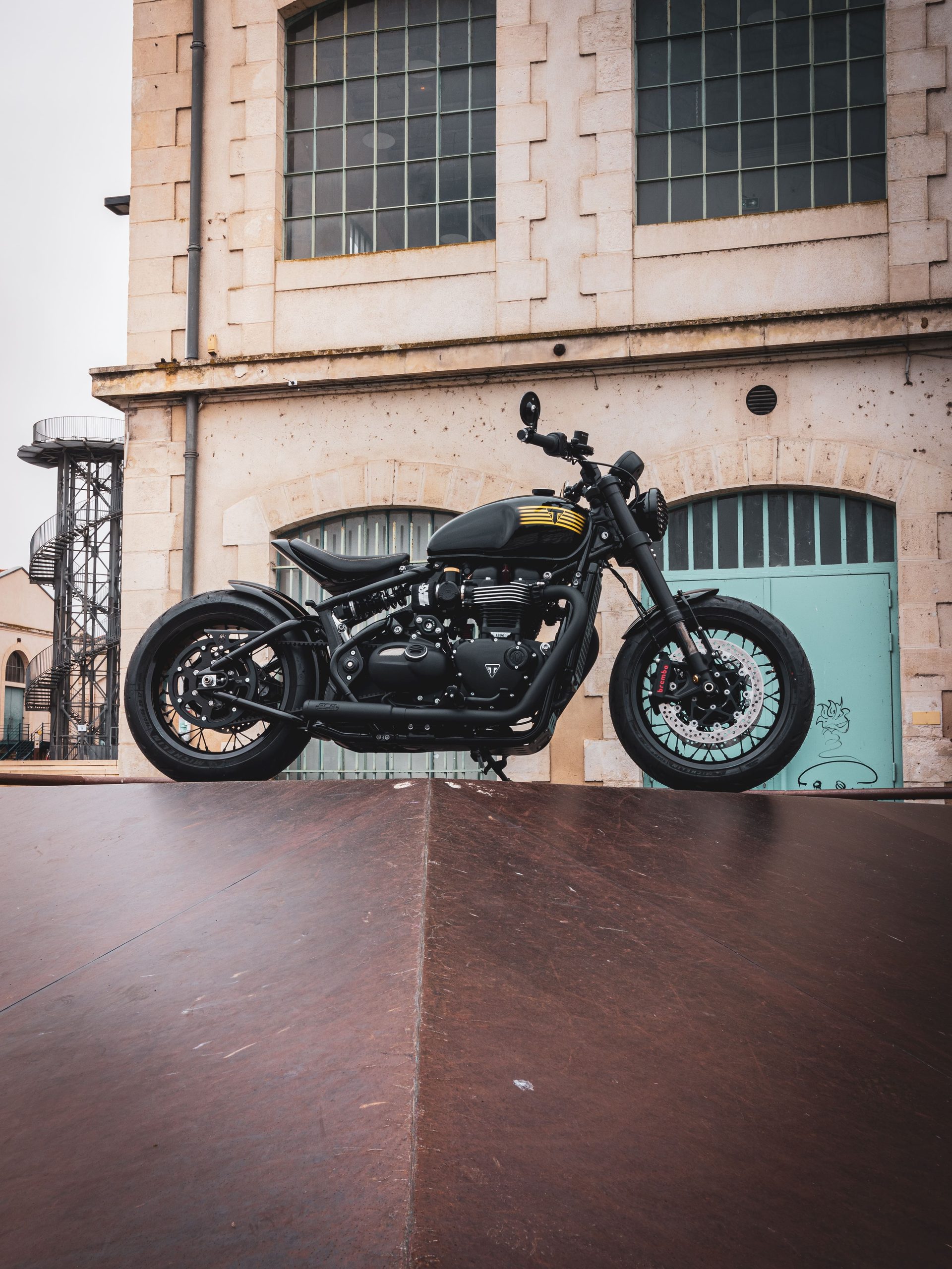 Préparation Triumph Bobber par FCR Original devant une façade industrielle