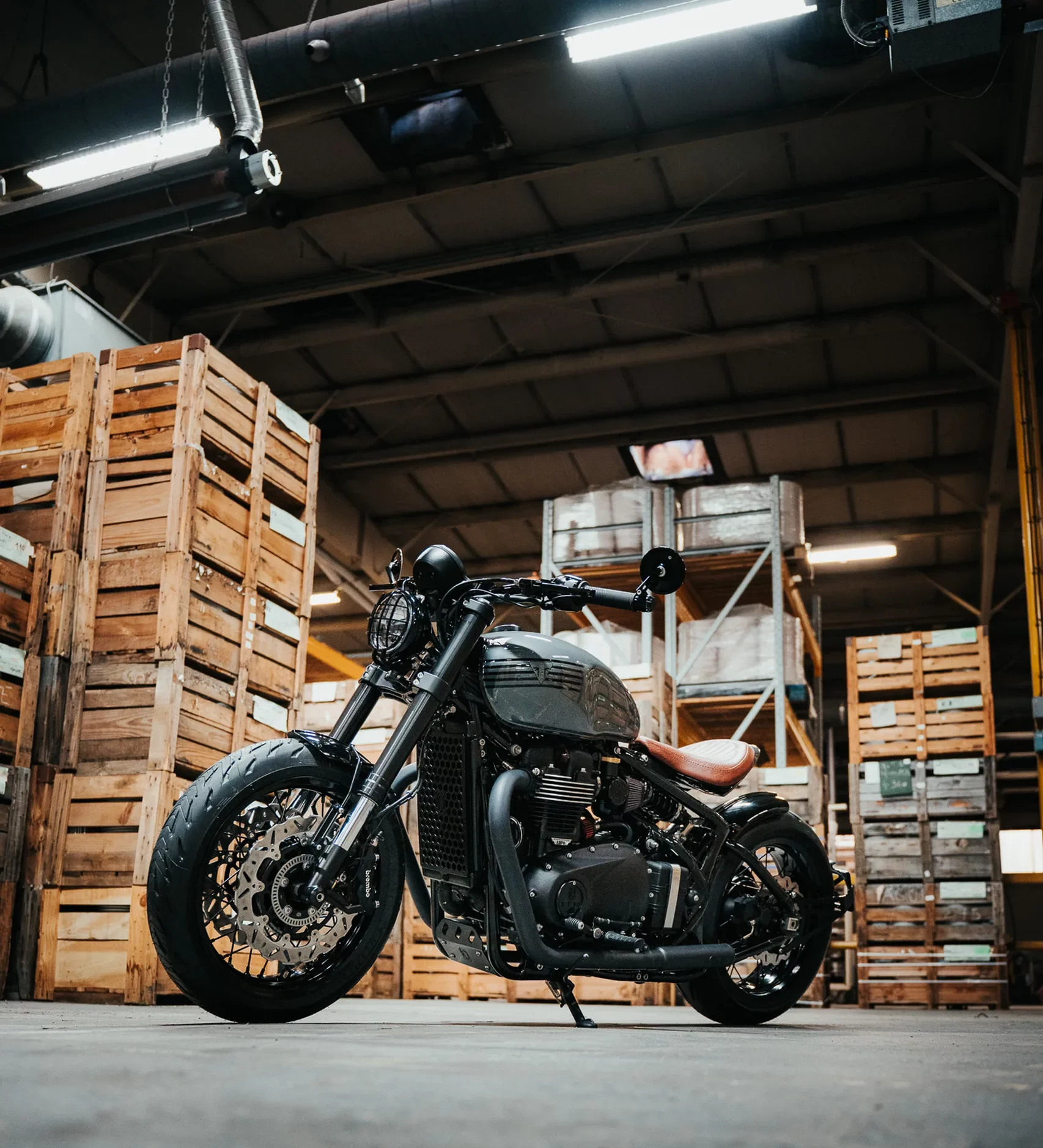 Triumph Bobber préparée par FCR Original dans un entrepôt de caisses en bois, esprit garage américain
