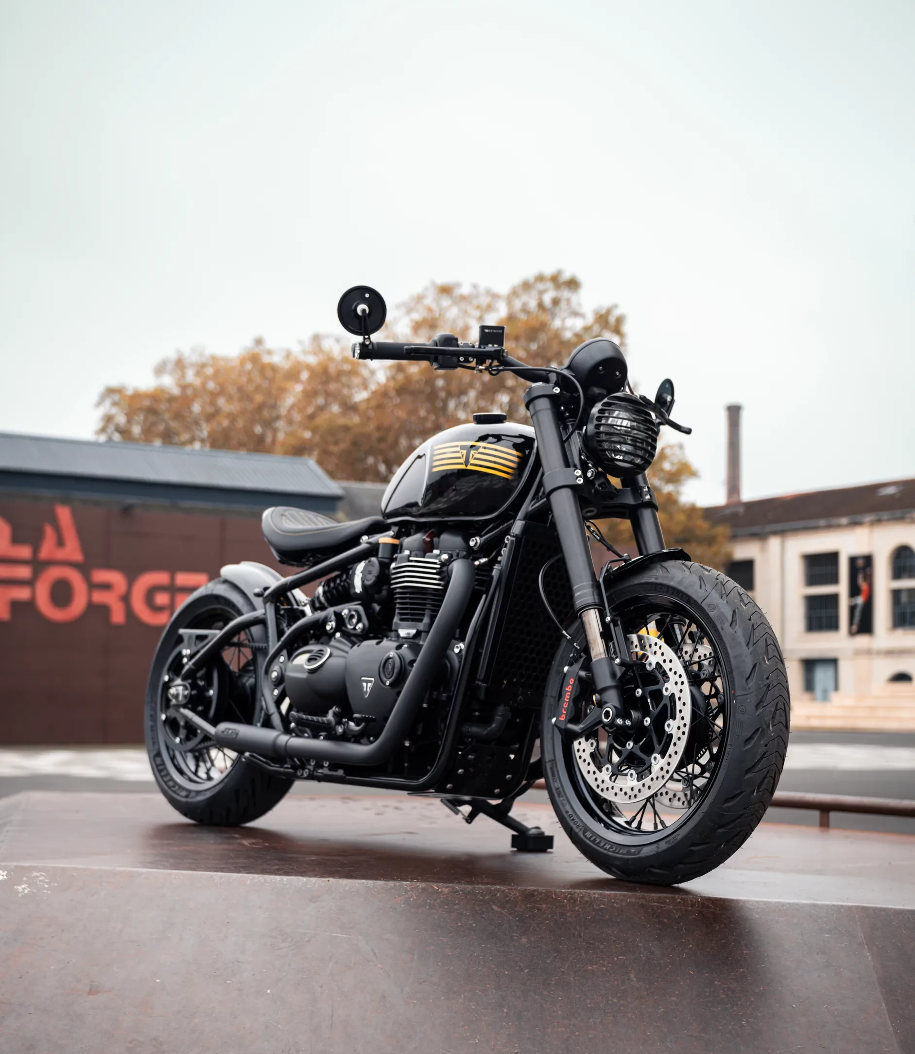 Triumph Bonneville 1200 Bobber préparée par FCR Original devant un bâtiment industriel