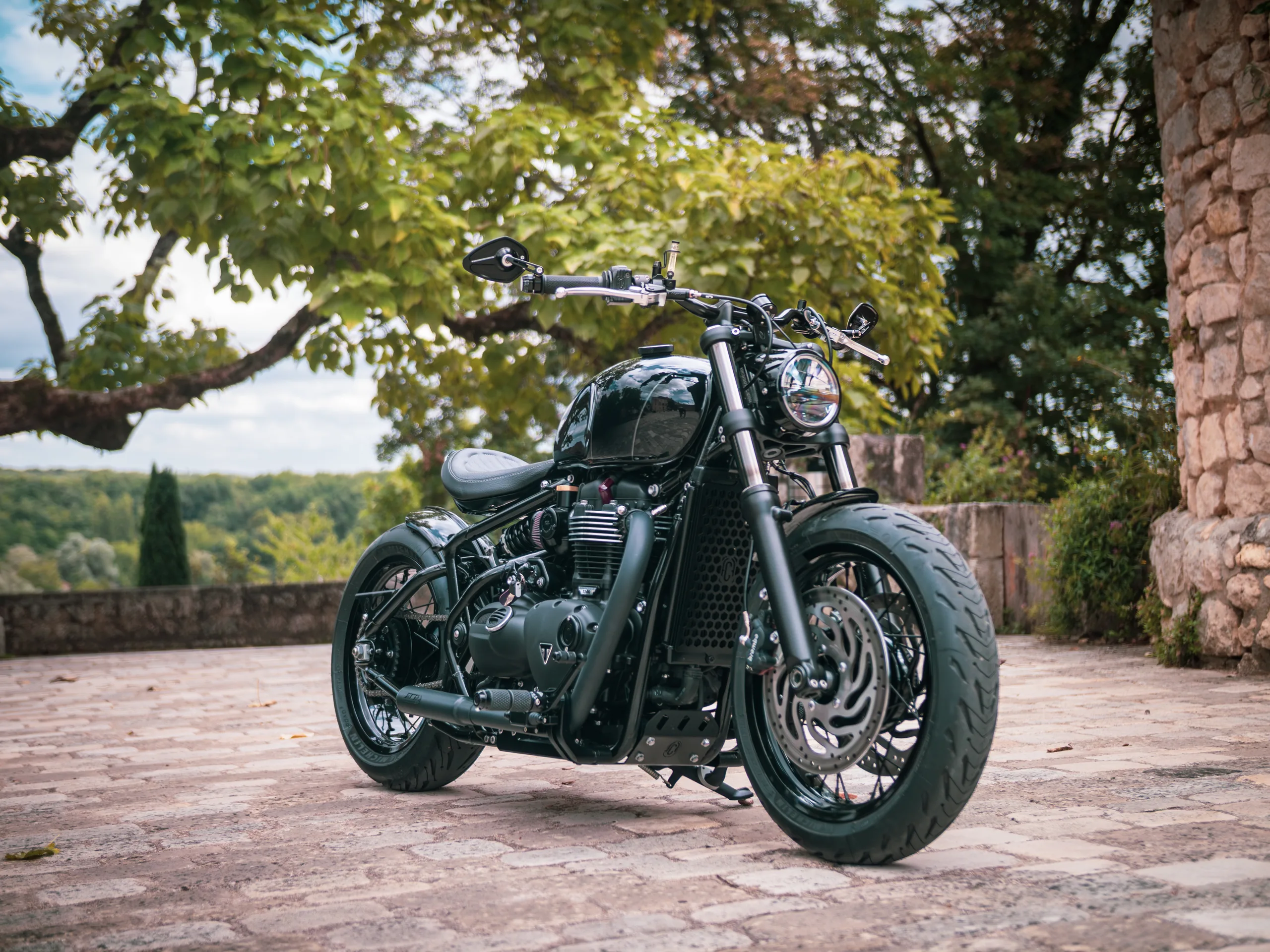 Bobber noir préparé par FCR Original sur une terrasse en pierre, silhouette basse et dépouillée